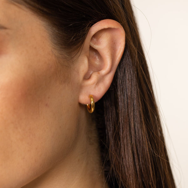 PURELEI Brave Ohrringe, glänzende 14K Gold Creolen, minimalistisch und elegant getragen am Ohr, femininer Island-Spirit.