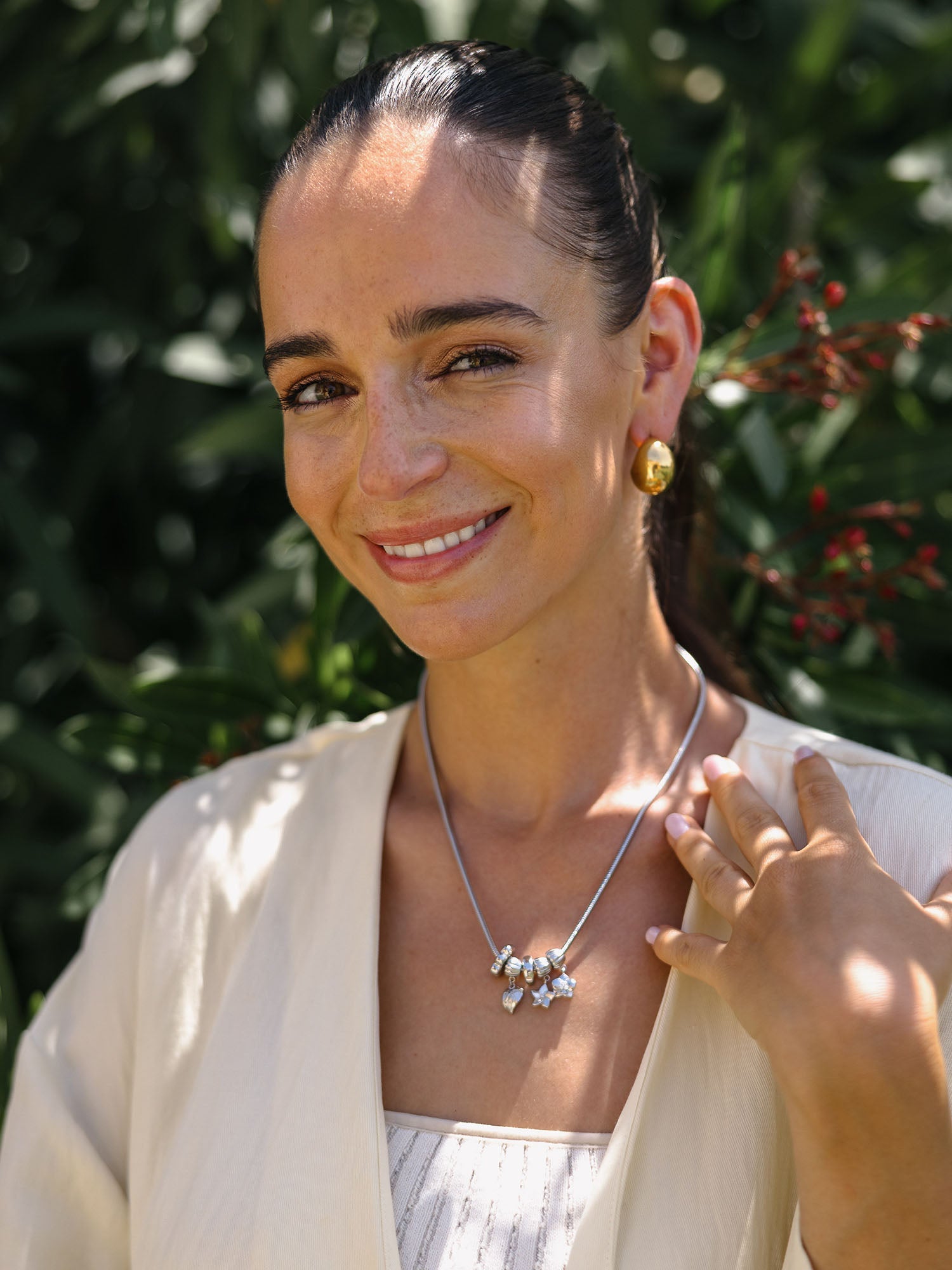 PURELEI Lei Flamingoblumen Charm in Gold mit herzförmiger Blüte, getragen vor tropischem grünem Hintergrund