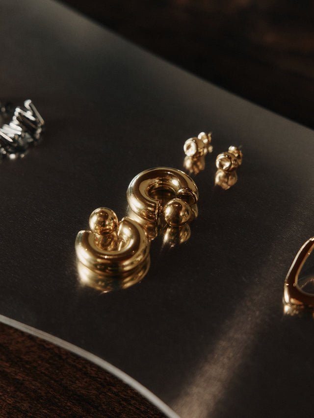 Goldene Ohrringe von PURELEI auf dunklem Untergrund, elegant und modern.