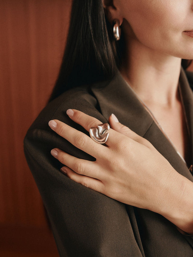 Eleganter Ring aus Roségold mit fließendem Design, getragen von einer Frau in einem stilvollen Outfit – PURELEI.
