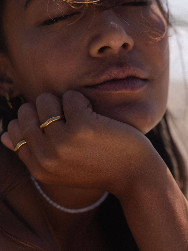 PURELEI Nakuna Ring in 18K Gold mit natürlicher Wellenform, getragen in warmem Sonnenlicht auf Haut nah am Gesicht