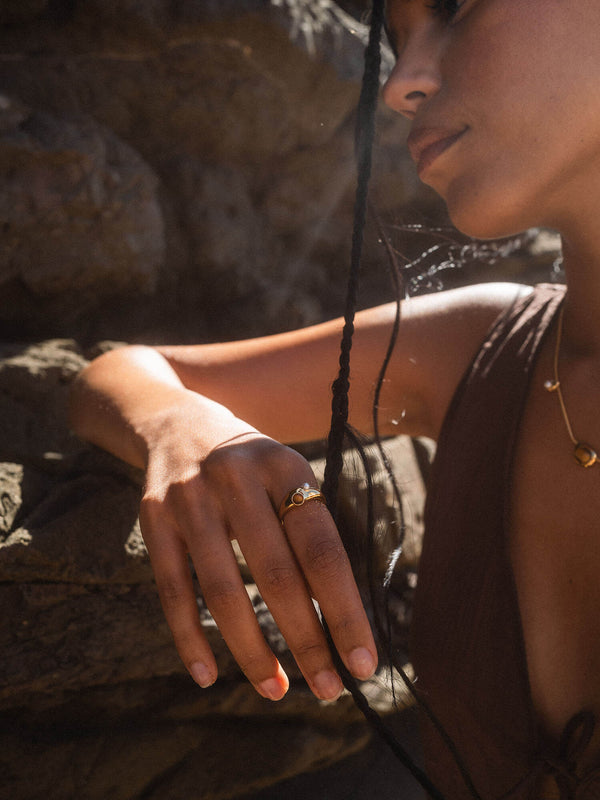 Goldener Ring mit rotem Stein, getragen in tropischer Atmosphäre, PURELEI inspiriert.