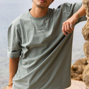 Mann in grauem Shirt mit PURELEI Kette und Ring, entspannte Strandstimmung.